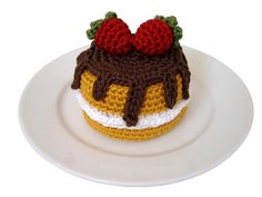 a crocheted cake with strawberries on top sits on a white platter