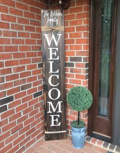 a welcome sign sitting on the side of a brick building next to a potted plant