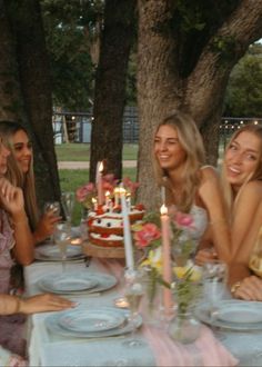 four women sitting at a table with a cake and candles in front of them,