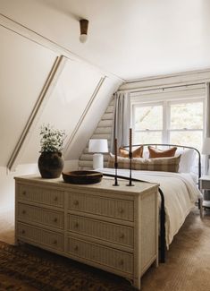 a bed sitting under a window in a bedroom next to a dresser and lamp on top of a rug