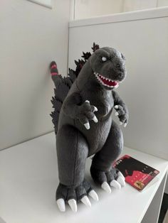 a stuffed toy godzilla sitting on top of a white table next to a red book