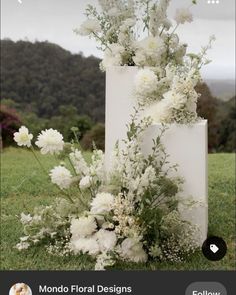 a tall white vase filled with flowers on top of a grass covered field next to trees