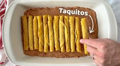 a white plate topped with a chocolate cake covered in yellow pastry sticks next to a hand pointing at it