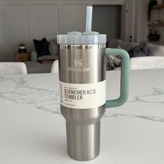 a stainless steel travel mug with a blue lid and handle sits on a white table