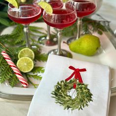 the table is set with three glasses of red wine, limes and christmas decorations