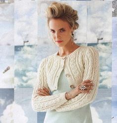 a woman in a white sweater and dress standing with her arms crossed, looking at the camera