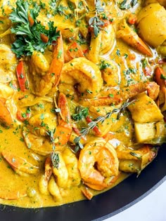 a skillet filled with shrimp and potatoes covered in yellow sauce, garnished with parsley