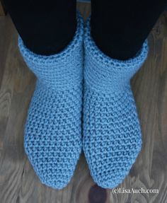 a pair of blue crocheted slippers on top of a wooden floor next to a person's feet