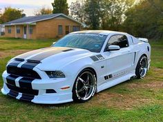 a white mustang parked on top of a grass covered field in front of a house