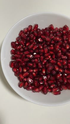 pomegranates in a white bowl sitting on a counter top, ready to be eaten