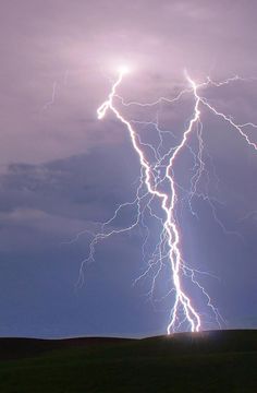 a lightning bolt is seen in the sky above a field with green grass and dark clouds