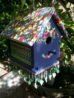 a blue birdhouse with flowers painted on it's roof and chains hanging from the side