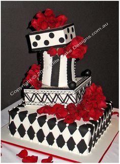 a three tiered cake with red roses on top and black and white design, sitting on a table