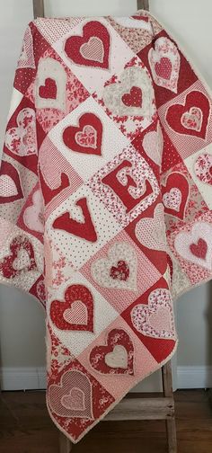 a red and white heart quilt sitting on top of a wooden chair next to a wall