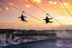 two people are suspended from wires above the water as they ride on snow covered skis