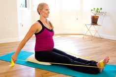 a woman is sitting on a yoga mat and stretching her legs with two yellow handles