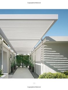 an outdoor covered walkway with plants and potted plants on either side, in front of a white building