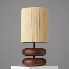 a wooden table lamp sitting on top of a white pedestal next to a beige lampshade