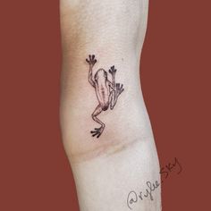 a small frog tattoo on the left side of the arm, with one foot in the air