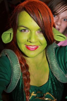 a woman with red hair and green makeup is posing for the camera while holding her hands behind her head