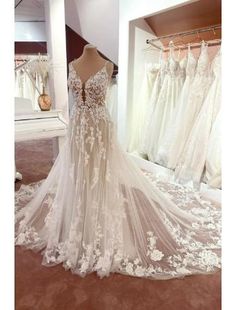 a wedding dress on display in front of a mirror with dresses hanging up behind it