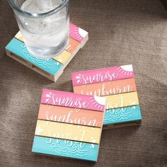 three square coasters with words on them and a glass of water in the background