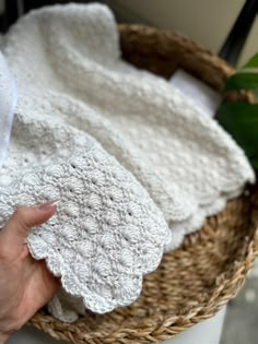 a person is holding some white crocheted towels in a basket next to a plant