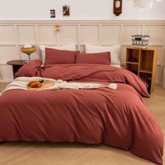 a bed with red sheets and pillows in a white room next to a wooden table