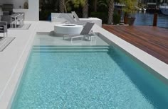 an empty swimming pool next to a deck with lounge chairs and a fire pit in the middle