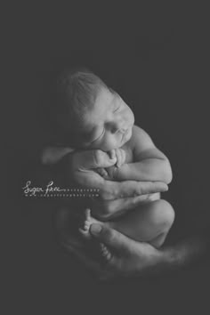 a black and white photo of a baby sleeping in his mother's arms with her hands