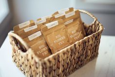 four bags of flower tea sit in a woven basket on a white countertop next to a window