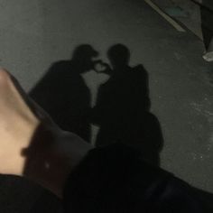 two people standing next to each other with their shadows on the ground and one person holding a cell phone