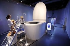 a woman standing on a ladder next to a giant toilet in a room with blue walls