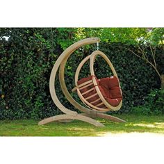 a wooden swing chair in the middle of a grassy area with trees and bushes behind it