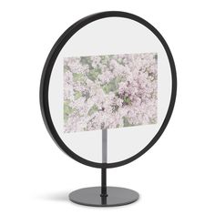 a round mirror with a black stand and white flowers on it