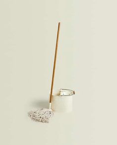 a white cup with a wooden handle and a mop on the floor next to it