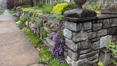 a stone wall with flowers growing on it and a statue in the middle next to it