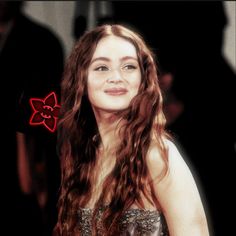 a woman with long brown hair wearing a silver dress and red flower clip in her hair