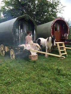 a woman standing next to two horses in front of a small train car on the grass