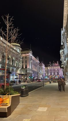 a city street at night with people walking on the sidewalk and buildings in the background