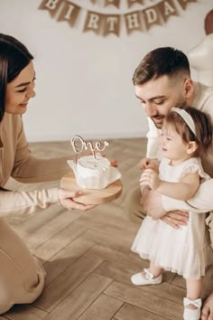 a man and woman holding a small child in front of a birthday cake