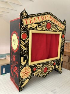 a cardboard box with a red curtain in the middle and an ornate design on it