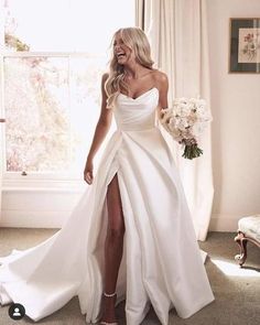 a woman in a white wedding dress standing next to a window with her legs crossed