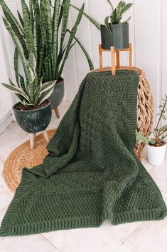 a green knitted blanket sitting on top of a rug next to potted plants