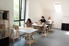 two women are sitting at desks in an office with books and papers on them