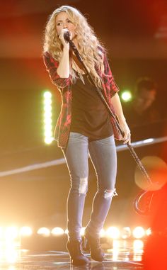 the singer is singing on stage with her microphone up to her ear and wearing ripped jeans