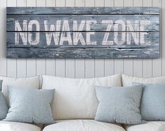 a wooden sign that says no wake zone hanging on a wall above a white couch