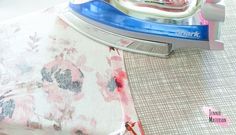 an iron sitting on top of a flowered pillow next to a pink and white pillow