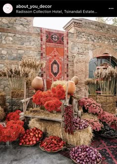 an assortment of vegetables and fruits on display in front of a brick building with red flowers