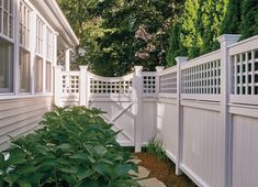 a white picket fence next to a house with trees in the back ground and bushes behind it